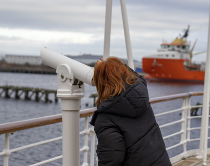 A visitor looks through a large white telescope on the Verandah Deck.