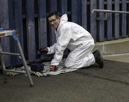A member of the Maintenance team is painting a wooden fence with dark blue paint. 