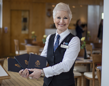 A waiter stands smiling as she holds leather bound Britannia menus waiting to greet visitors.  