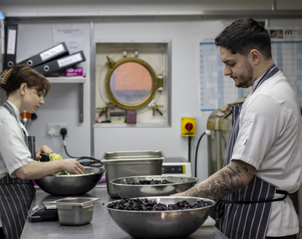 Chefs in the onboard galley preparing fruit in large bowls to make Christmas puddings. 