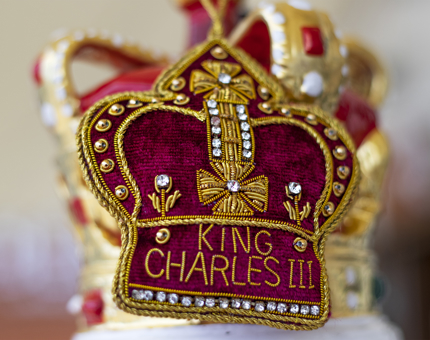 A soft red and gold crown decoration embroidered with King Charles III. 