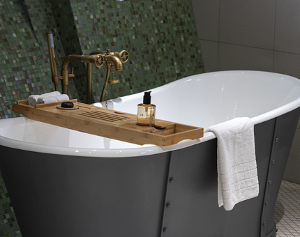 A roll-top bath within one of Fingal's beautiful duplex cabins. A towel is draped across the bathtub and a green mosaic wall is in the background. 