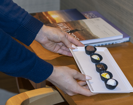 A Housekeeper places a tray of handmade chocolates in a cabin ready for a new guest's arrival. 