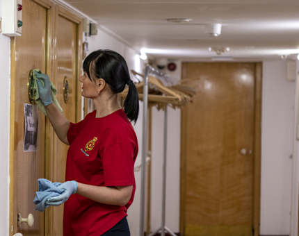 A Housekeeper polishing a porthole on a door. 