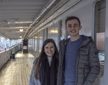 A woman and a man stand next to each other smiling as they stand outside the State Apartments on board Britannia. 
