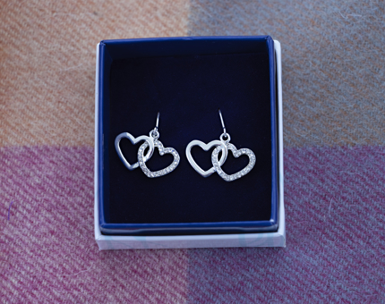 A small jewellery gift box containing a pair of interlocking heart-shaped silver diamanté earrings. 