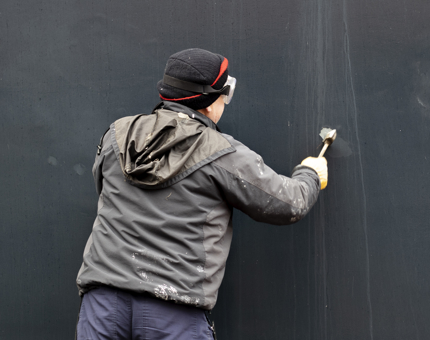 A team member wearing protective goggles standing at the hull as he holds a tool working at an area of the paintwork. 