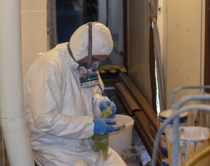 A man wearing protective clothing and a mask holding a spray painting gun as he prepares to spray paint. 