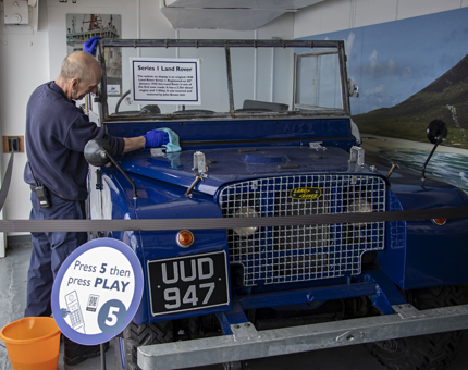 A member of the Facilities Team cleaning a deep blue 1948 Series 1 Land Rover. 