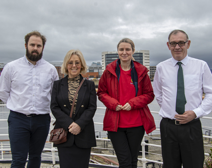 Four members of Britannia and Fingal staff, two men and two women, standing on Fingal smiling. 