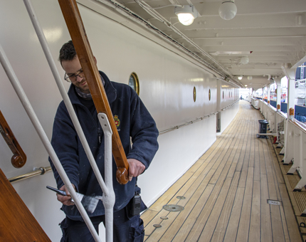 A member of the Maintenance team painting handrails on the Shelter Deck.