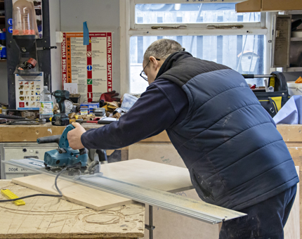 A man holding a sawing machine working in the workshop. 
