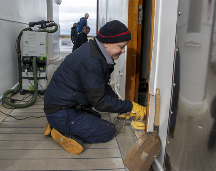A Maintenance man sanding a doorframe. 