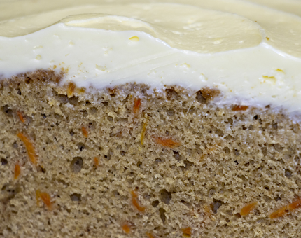 A close-up of a slice of carrot cake showing the sponge filling with shredded carrot and frosted layer on top.