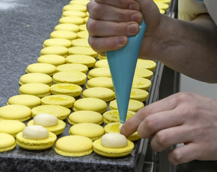 A chef piping the filling into a row of yellow macarons in the onboard Galley. 