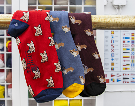 Three pairs of socks with miniature corgi designs printed hang over a rail.