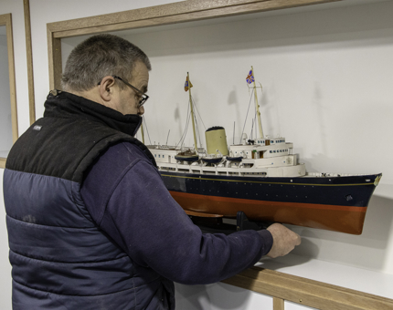A man positioning the Britannia model in the display cabinet in the former Junior Rates' Dining Hall. 