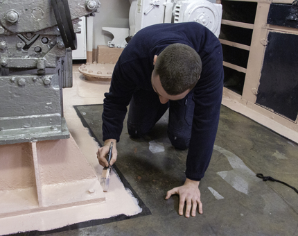 A man kneeling holding a paintbrush as he applies an undercoat to the deck. 