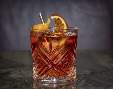 A short glass tumbler containing a negroni cocktail with a twist of lemon and orange. 