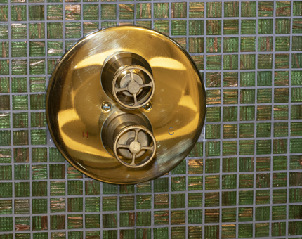 Brass detail within the shower at Fingal with a blue-green mosaic shimmering tiled background. 