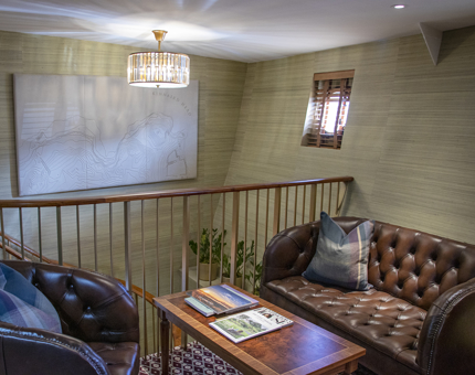 The upstairs level of a duplex cabin at Fingal with a leather sofa, armchair and coffee table laid with magazines.