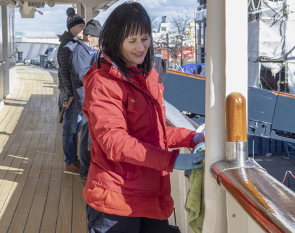 A Housekeeper woman polishing a wooden handrail on the Shelter Deck at Britannia. 