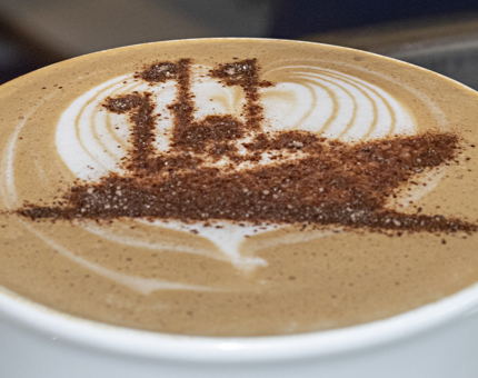 A close-up of the top of a flat white drink with a Britannia outlined stencil. 