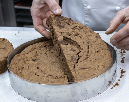 A chef slicing a tin filled with a chocolate brownie dessert.
