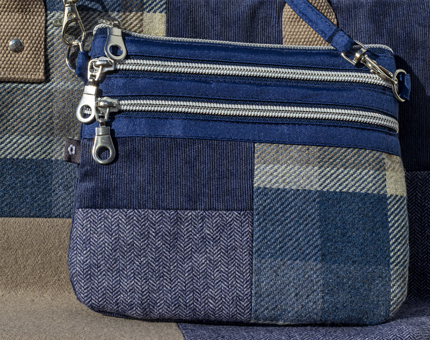 A blue patchwork tweed cross body bag sits on a tote bag. 
