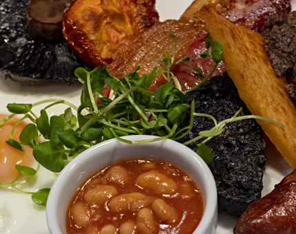 A close-up of a full Scottish breakfast with egg, mushroom, tomato, bacon, black pudding, hash brown, haggis, sausage and baked beans. 