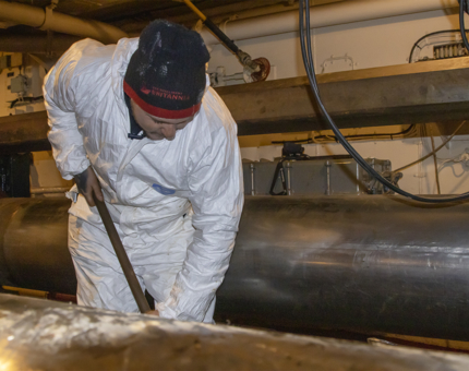 A man wearing white overalls removing rust spots on the deck. 
