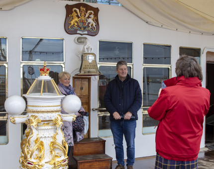 Two visitors posing for a photograph on the Verandah Deck as a Visitor Assistant takes their picture. 