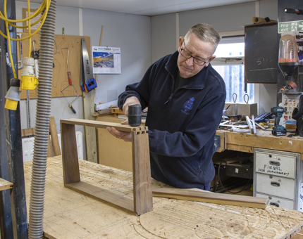 A man making a wooden box for the instrument panel on the helm at Bloodhound.