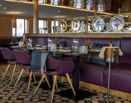 The inside view of The Lighthouse Restaurant & Bar with tables laid for dinner. There is a booth with chairs sitting opposite the table and a champagne bucket.