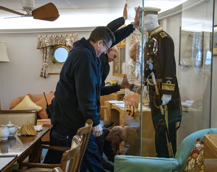 All three members of Britannia's Facilities team installing the Admiral's uniform in a glass case inside the Admiral's Suite.