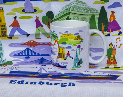 A mug featuring a brightly coloured design of Edinburgh landmarks sitting on a tea towel with the same design. 