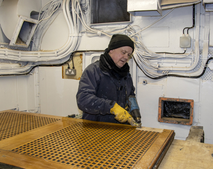 A man holding tools to remove varnish from a blanket box. 