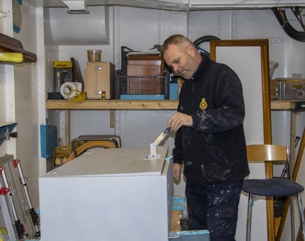 Maintenance man applying paint to a storage cabinet in the workshop. 