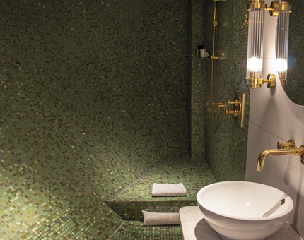 Inside a duplex cabin's bathroom at Fingal. The walls are tiled with green mosaic and the wash basin and mirror have nautical-style lighting. 