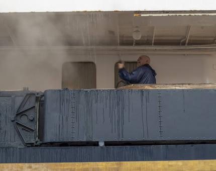 A member of the Maintenance team hosing the deckhead on the Shelter Deck using a powerwash. 