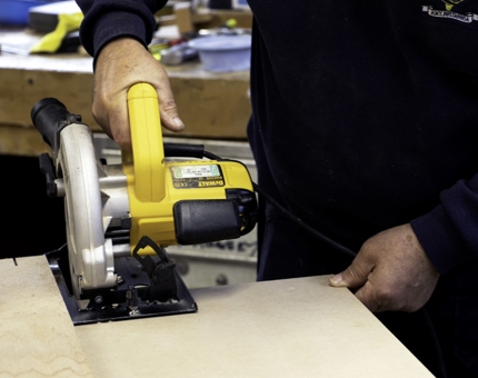 A close up of a member of the team using a piece of equipment in the workshop to cut out a board. 