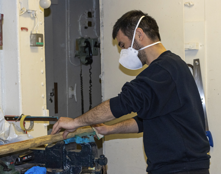 A member of the Maintenance team rounding boat hook ends. 