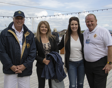 Two Yotties stand next to two women visitors posing on the Verandah Deck. 