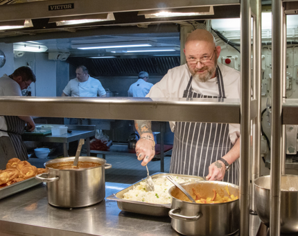 A Yottie Chef preparing a rice dish for lunch in the Galley. There are other Chefs working behind him. 