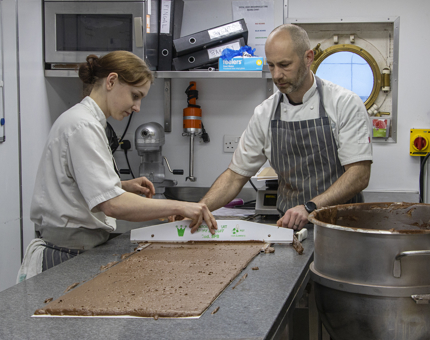 Two Pastry Chefs preparing chocolate sponge in the Galley. 