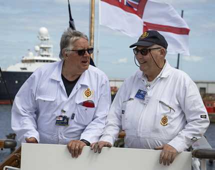 Two Yotties standing sharing a joke. They are wearing their white Royal Yachtsmen overalls. 