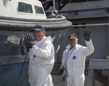 Two member of the Royal Yachtsmen waving at the camera as they pause during their work on the Fast Motor Launch.