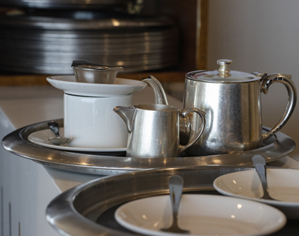 A tea tray containing a silver teapot, milk jug, tea strainer, cups and saucers on the bar in the Royal Deck Tea Room. 