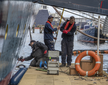 Three members of the Maintenance team sanding the hull of Britannia. 