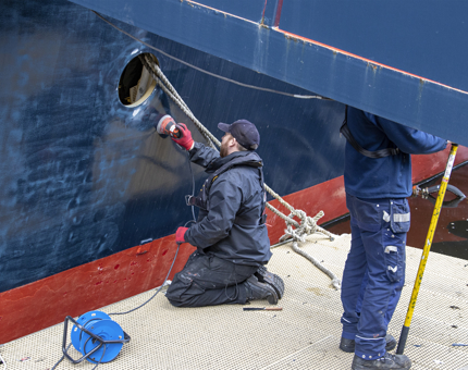 A man kneeling on a platform sanding Britannia's hull. 